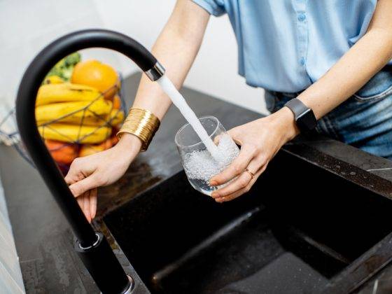 Woman filling glass with tap water for drinking on the kitchen