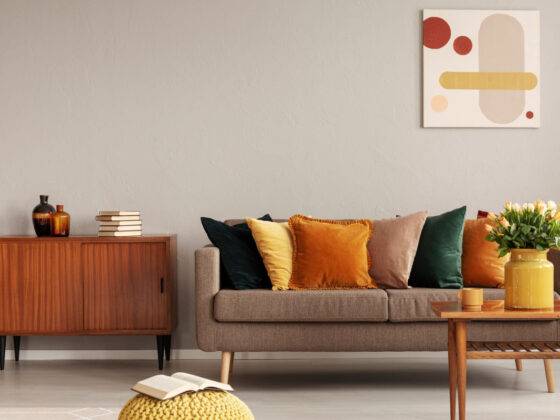 Books and vases on retro cabinet next to comfortable sofa with pillows