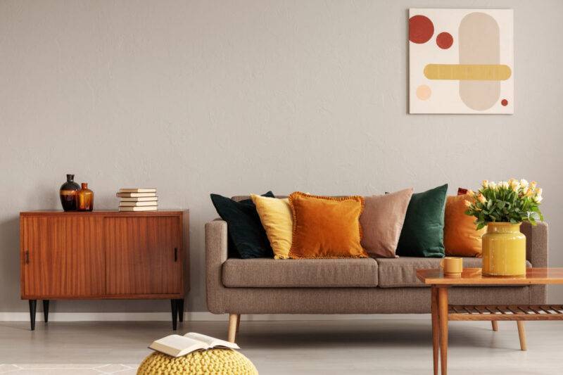 Books and vases on retro cabinet next to comfortable sofa with pillows